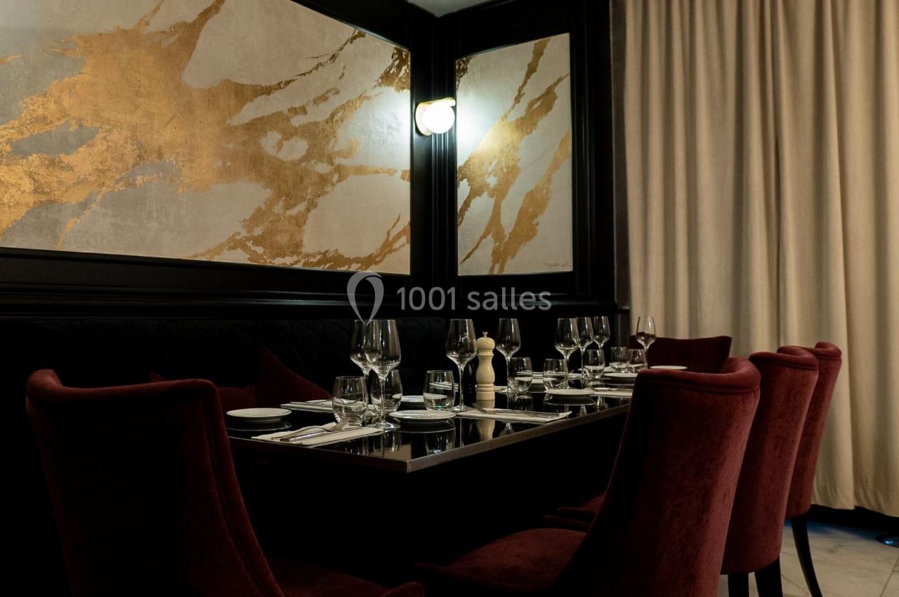 Salle de restaurant élégante avec table dressée, chaises en velours rouge et décor mural doré.