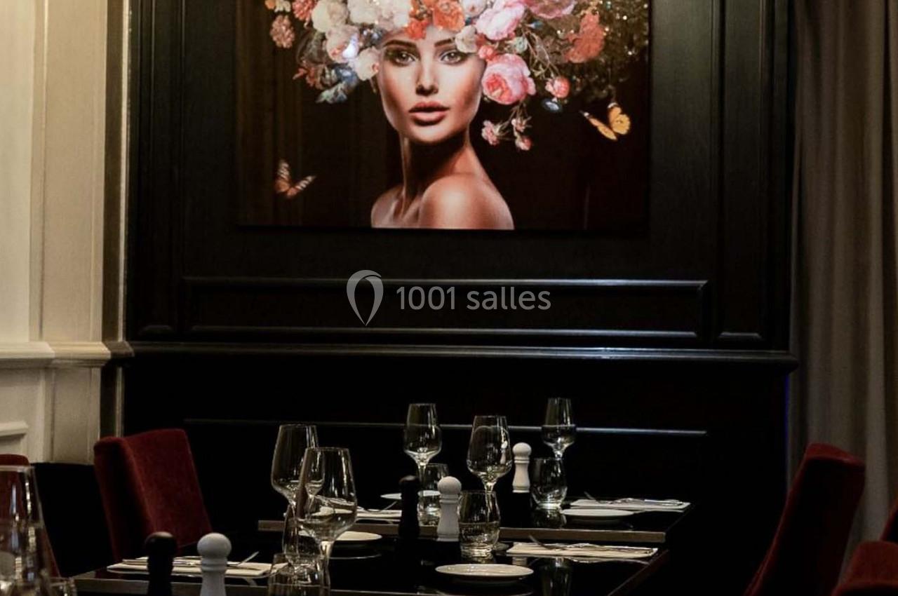 Table dressée dans un restaurant élégant avec un tableau représentant une femme ornée de fleurs en arrière-plan.