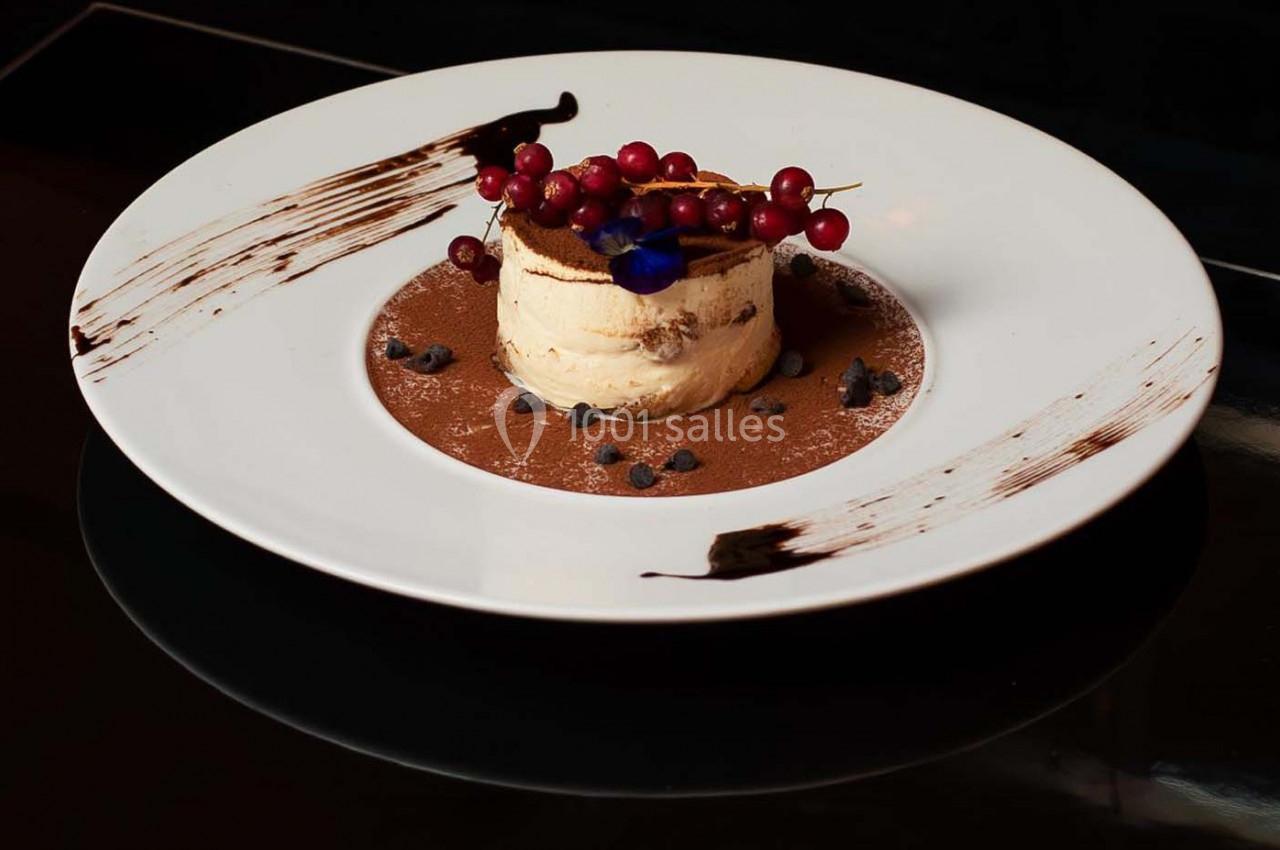 Dessert dressé sur une assiette blanche, avec mousse, cacao, groseilles rouges et décorations de chocolat.