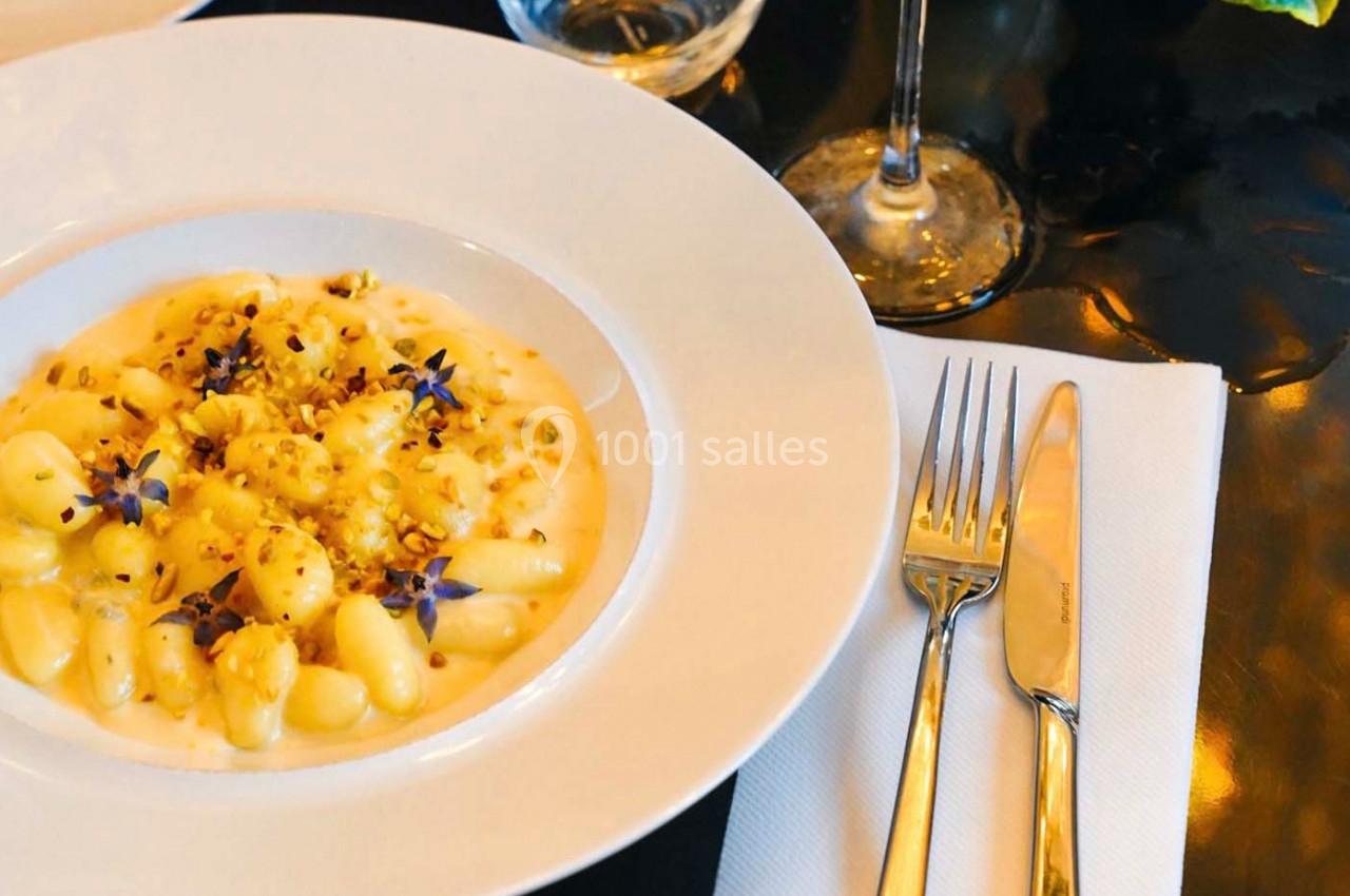 Assiette de gnocchis crémeux garnis de fleurs comestibles et éclats de noix, servie sur une table élégante.