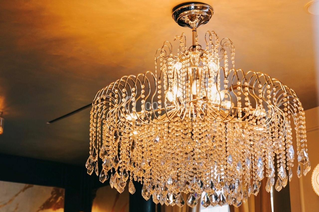 Lustre en cristal suspendu, éclairé, avec des pampilles étincelantes dans une pièce au plafond doré.