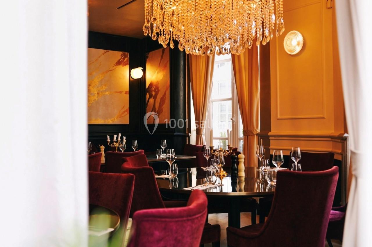 Salle de restaurant élégante avec chaises en velours rouge, table dressée et grand lustre en cristal suspendu.