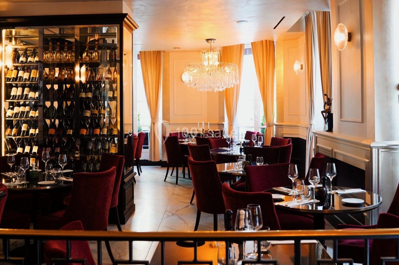 Salle de restaurant élégante avec chaises rouges, tables dressées et éclairage chaleureux sous un lustre.