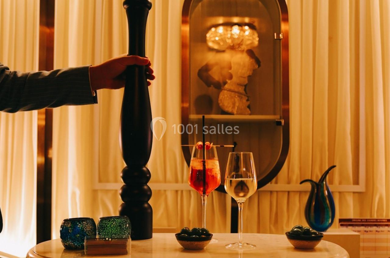 Un serveur ajuste un moulin à poivre près d'une table dressée avec des verres de cocktail et des olives dans un décor…