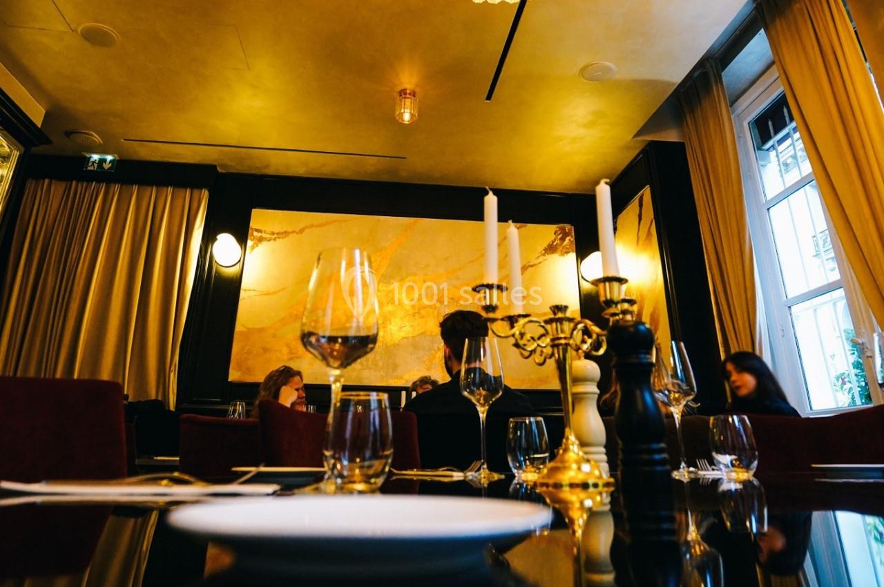 Salle de restaurant élégante avec tables dressées, chandeliers, rideaux beiges et éclairage chaleureux.