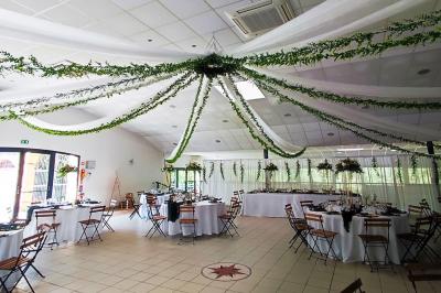 Ardoise décorative accrochée à une grille en fer forgé, entourée de végétation et d'un voile blanc.