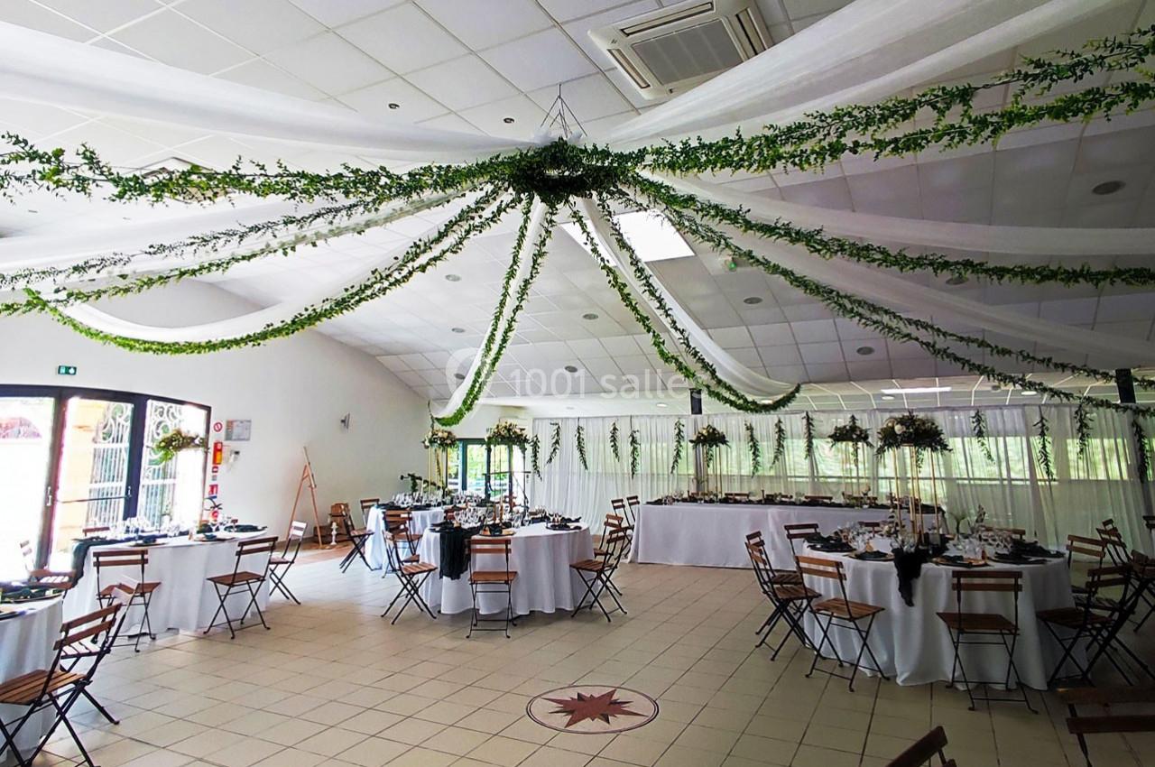 Salle de réception décorée avec des guirlandes végétales suspendues et des tables dressées pour un événement.