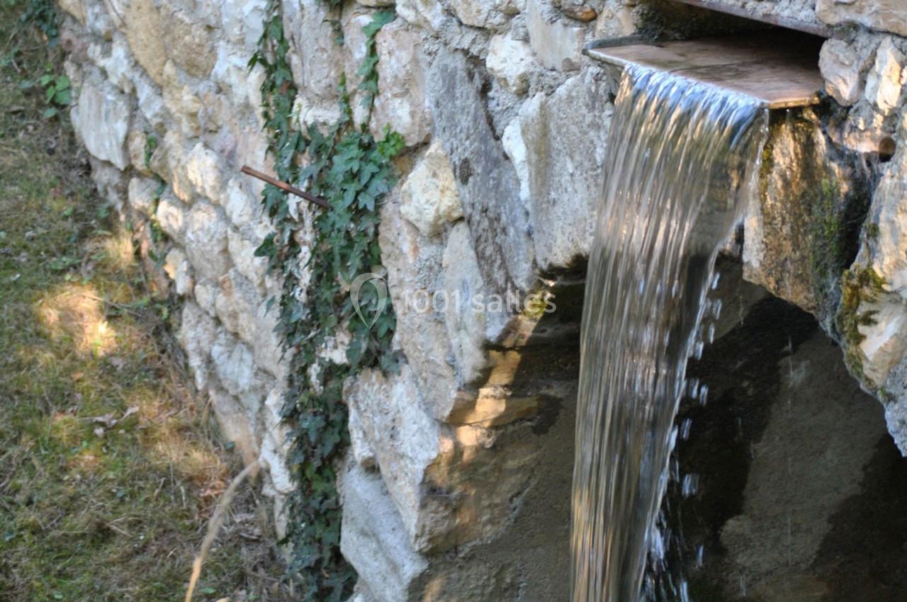 Eau s'écoulant d'un petit canal en pierre intégré à un mur, entouré de végétation.