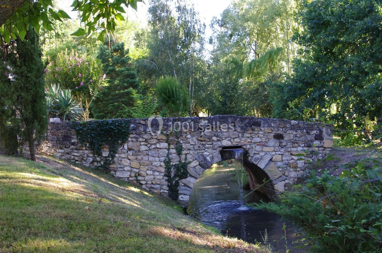 Pont en pierre ancien enjambant un petit cours d'eau entouré de végétation verdoyante.