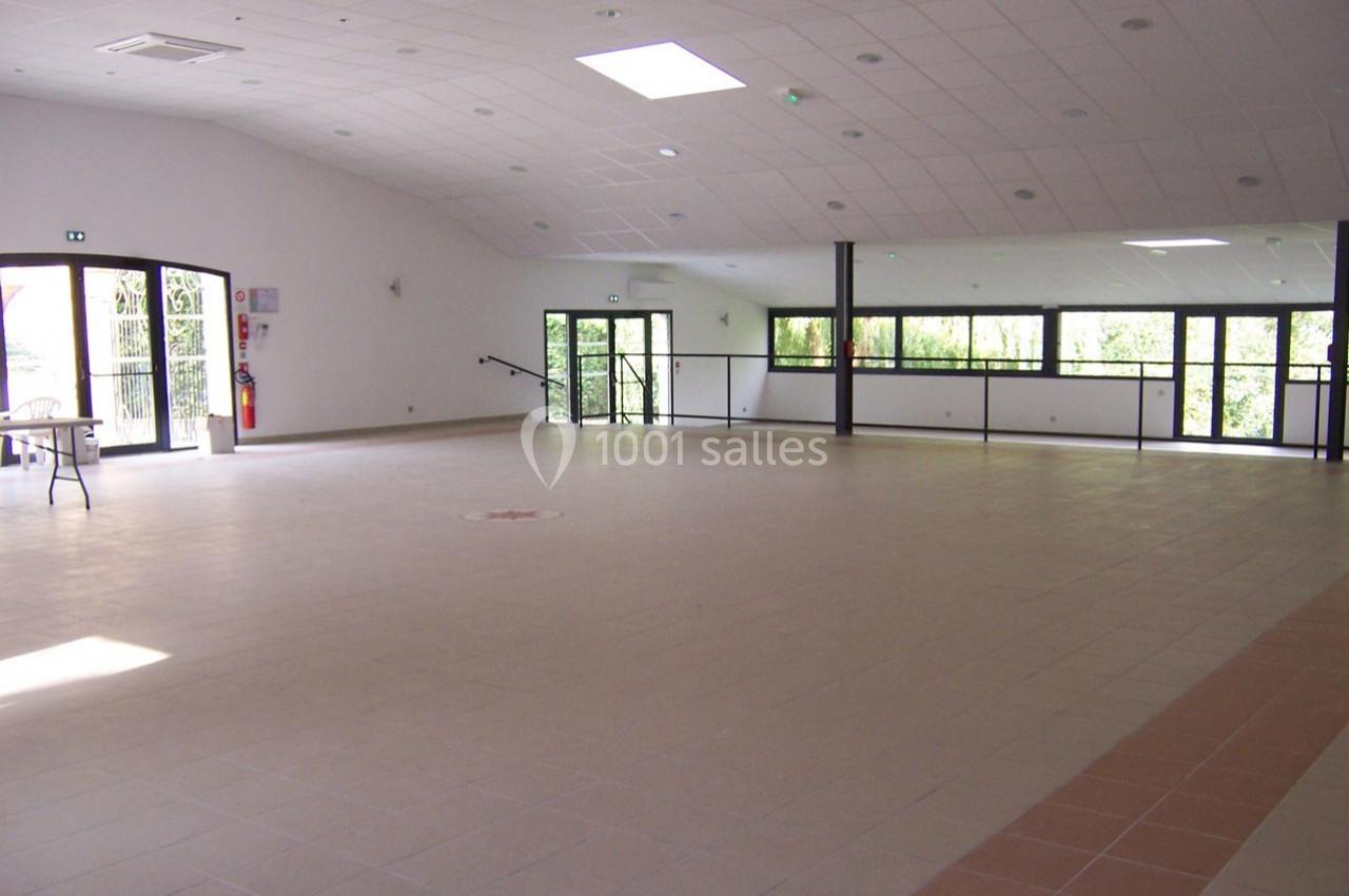 Salle vide avec sol carrelé, murs blancs, grandes fenêtres laissant entrer la lumière naturelle et plafond incliné.