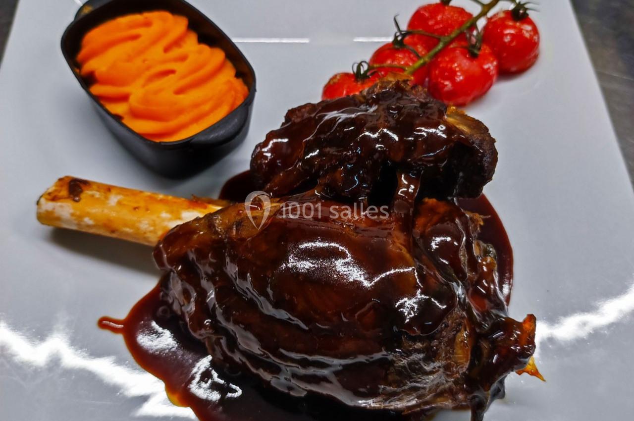 Jarret d'agneau nappé de sauce brune, accompagné de purée de patate douce et de tomates cerises rôties.