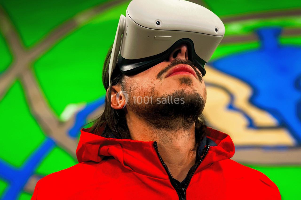 Un homme portant un casque de réalité virtuelle regarde vers le haut, devant un fond coloré abstrait.