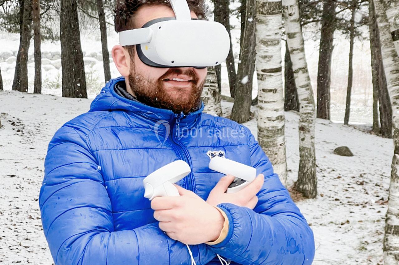 Un homme portant un casque de réalité virtuelle et tenant des manettes, debout dans une forêt enneigée.