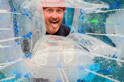 Une personne en combinaison rouge se tient devant un groupe d'adultes et d'enfants sur une aire extérieure.