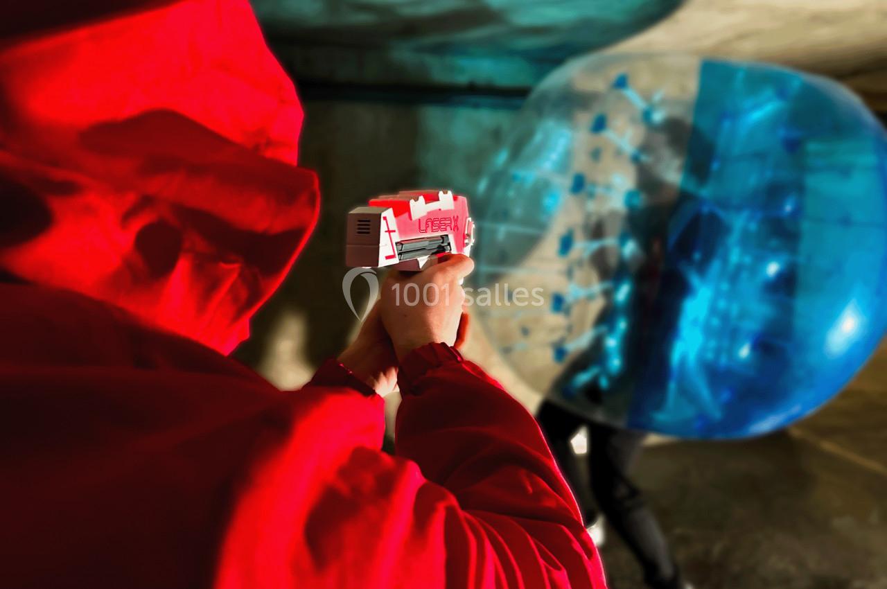Personne en veste rouge tenant un pistolet laser, visant une bulle gonflable bleue dans un espace intérieur.