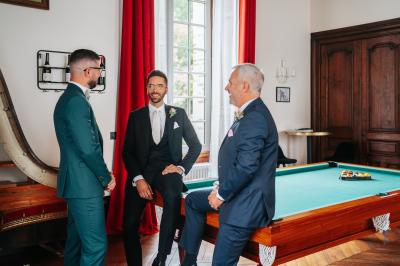 Salle spacieuse avec canapés, baby-foot, table de jeux et grandes fenêtres donnant sur un extérieur arboré.