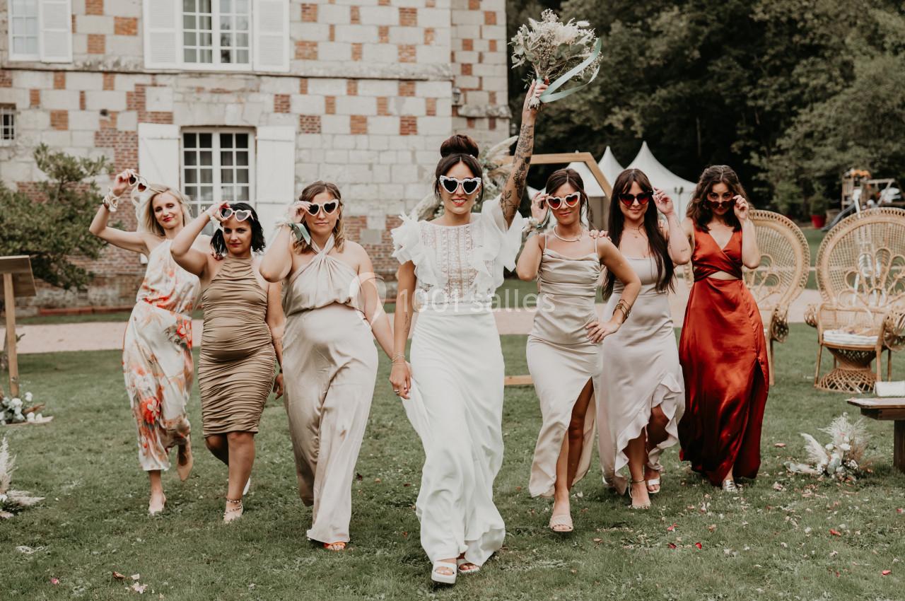 Un groupe de femmes en robes élégantes marche sur une pelouse devant un bâtiment en briques, portant des lunettes fantaisie.