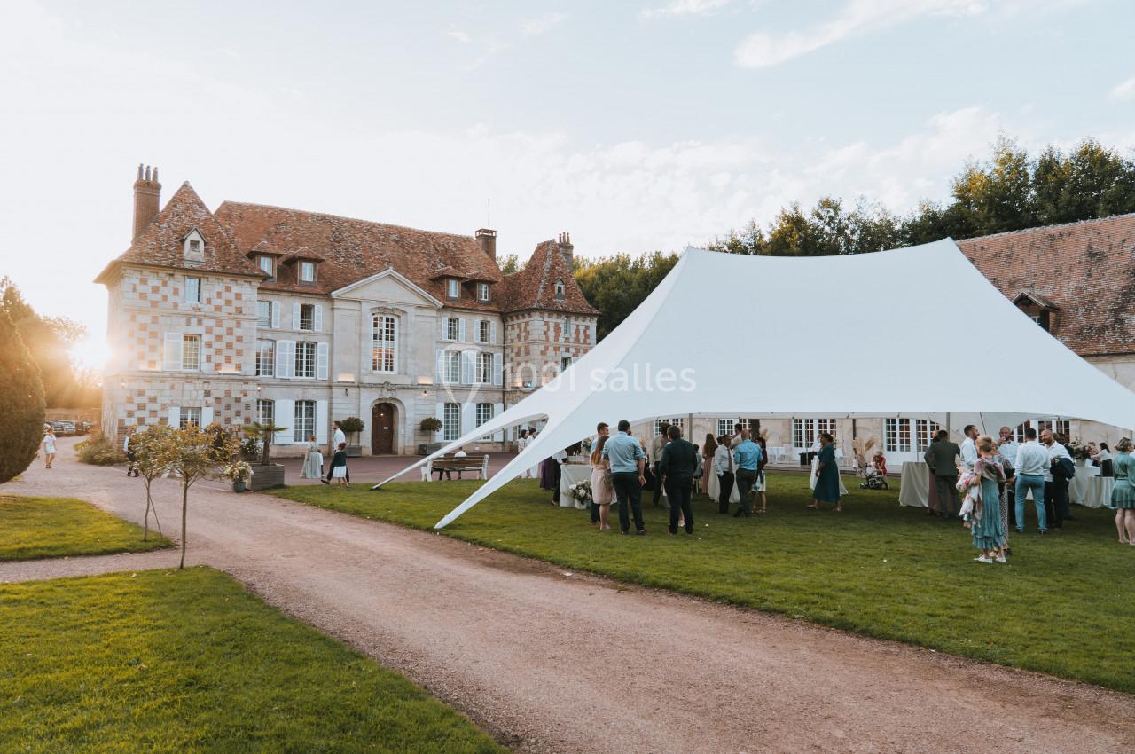 Tente blanche dressée dans le jardin d'un manoir en pierre, avec des invités rassemblés lors d'un événement en plein air.