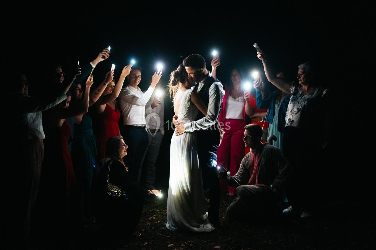 Un couple s'embrasse au centre d'un cercle de personnes éclairant la scène avec des lumières dans l'obscurité.