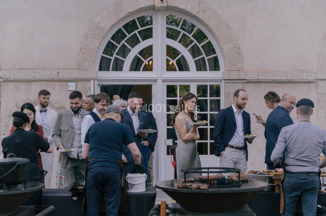 Des personnes rassemblées devant un bâtiment avec des assiettes, près de barbecues en extérieur.