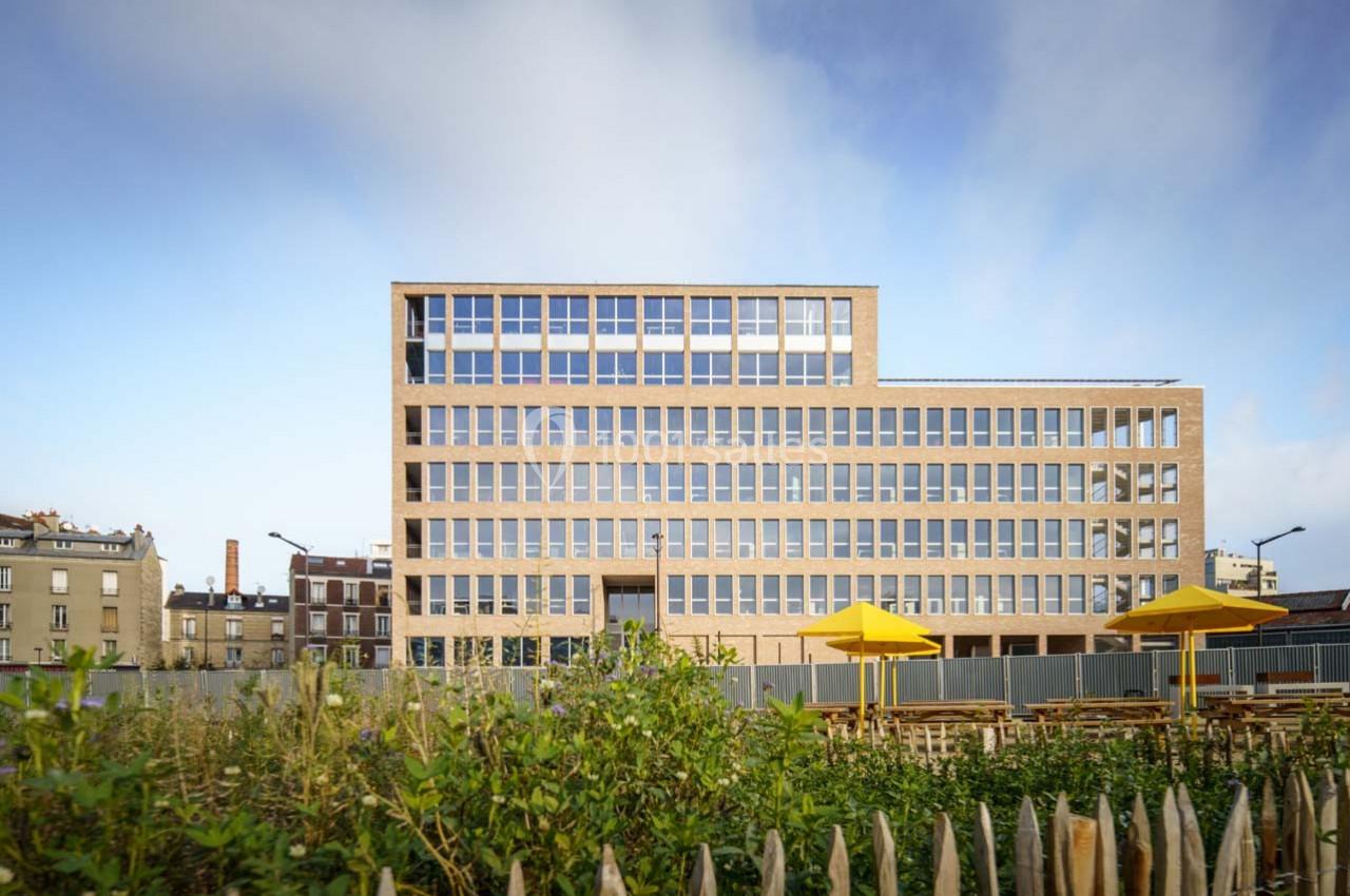 Bâtiment moderne en briques avec de grandes fenêtres, entouré de végétation et de parasols jaunes au premier plan.