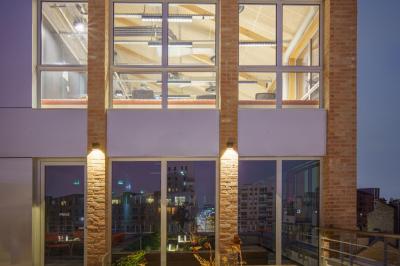 Façade d'un bâtiment moderne avec grandes baies vitrées illuminées, laissant entrevoir un intérieur aménagé.