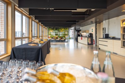 Salle de réunion moderne avec deux grandes tables en bois, chaises orange et baies vitrées donnant sur des bâtiments urbains.