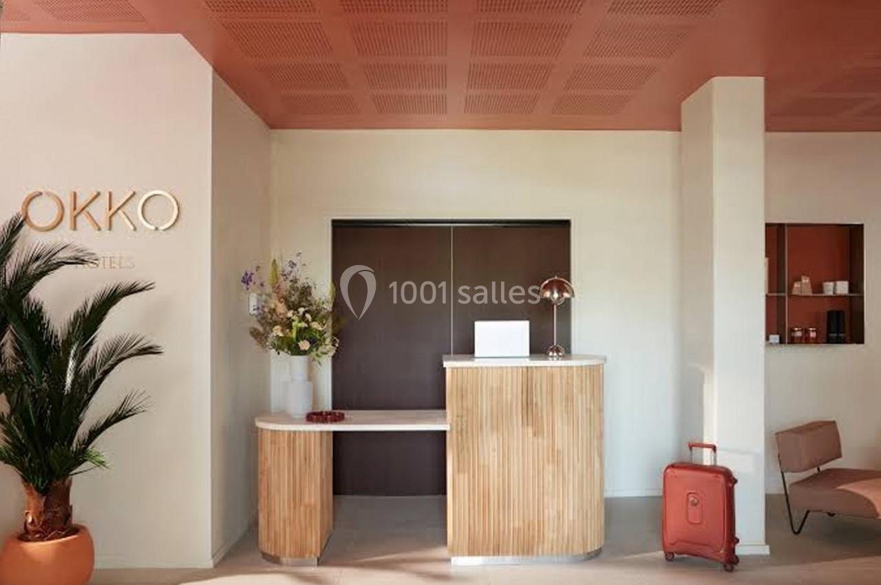 Réception d'un hôtel moderne avec comptoir en bois, valise rouge au sol et décoration minimaliste.