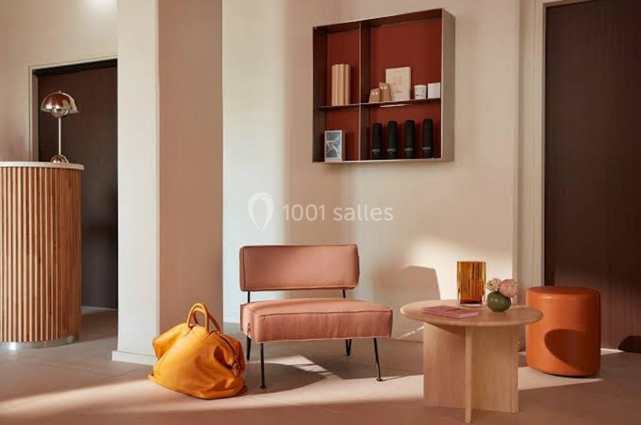 Espace intérieur moderne avec fauteuil rose, table basse en bois, sac orange et étagère murale décorative.