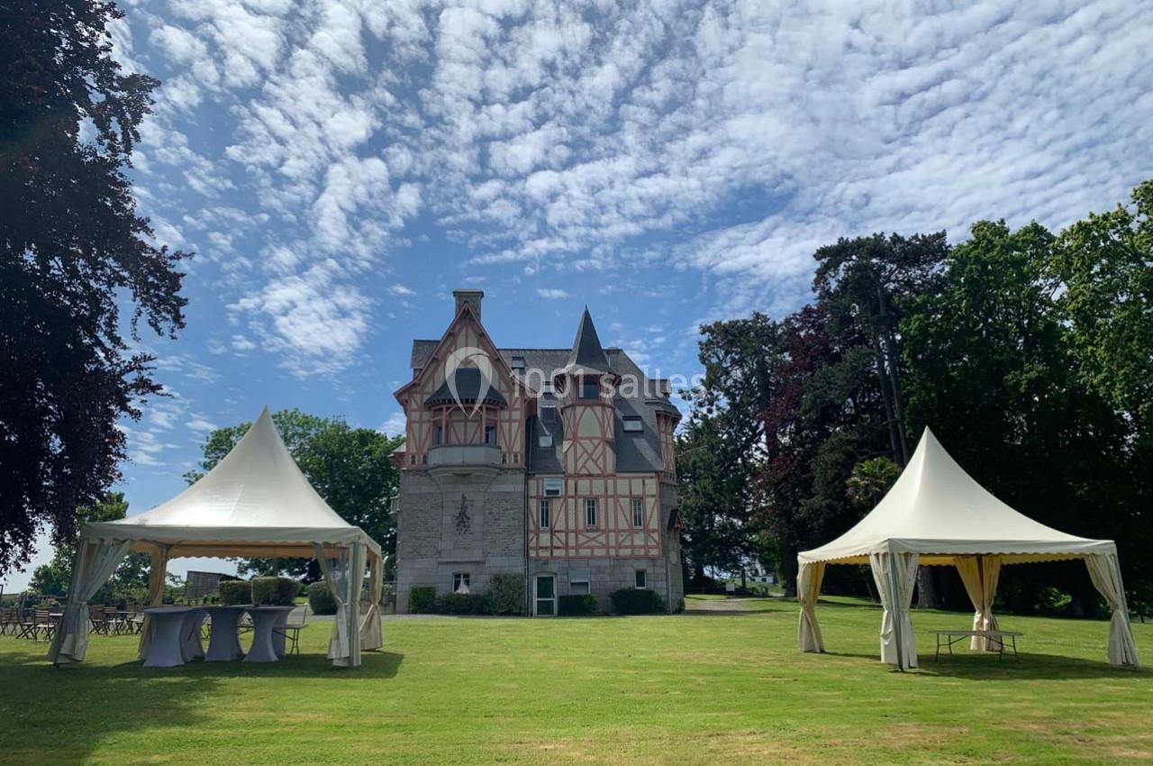 Deux tentes blanches installées sur une pelouse devant un bâtiment ancien à colombages sous un ciel partiellement nuageux.