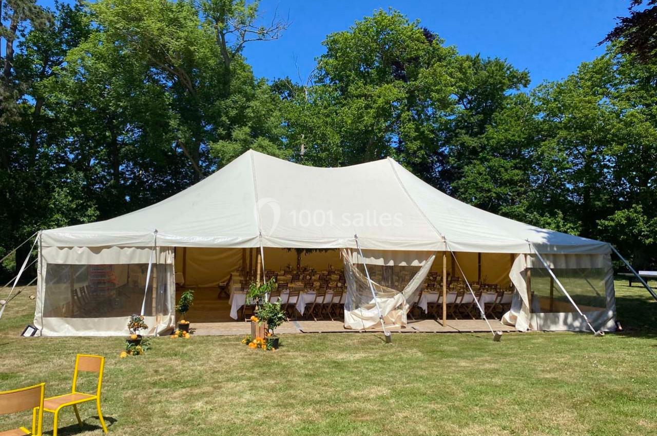 Grande tente blanche installée sur une pelouse, ouverte sur l'avant, avec des chaises et des décorations à l'intérieur.