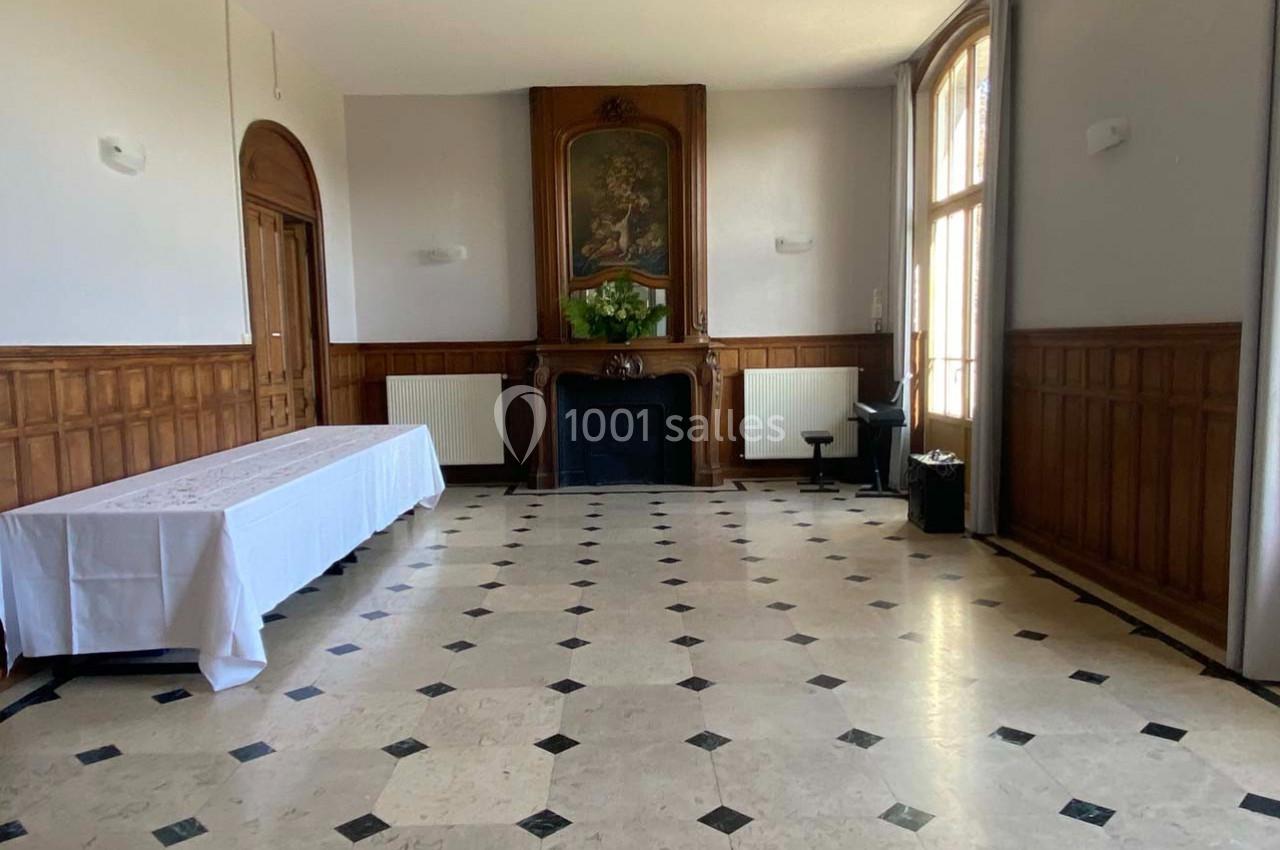 Salle lumineuse avec sol en marbre, murs en bois, cheminée décorative et grande fenêtre laissant entrer la lumière naturelle.