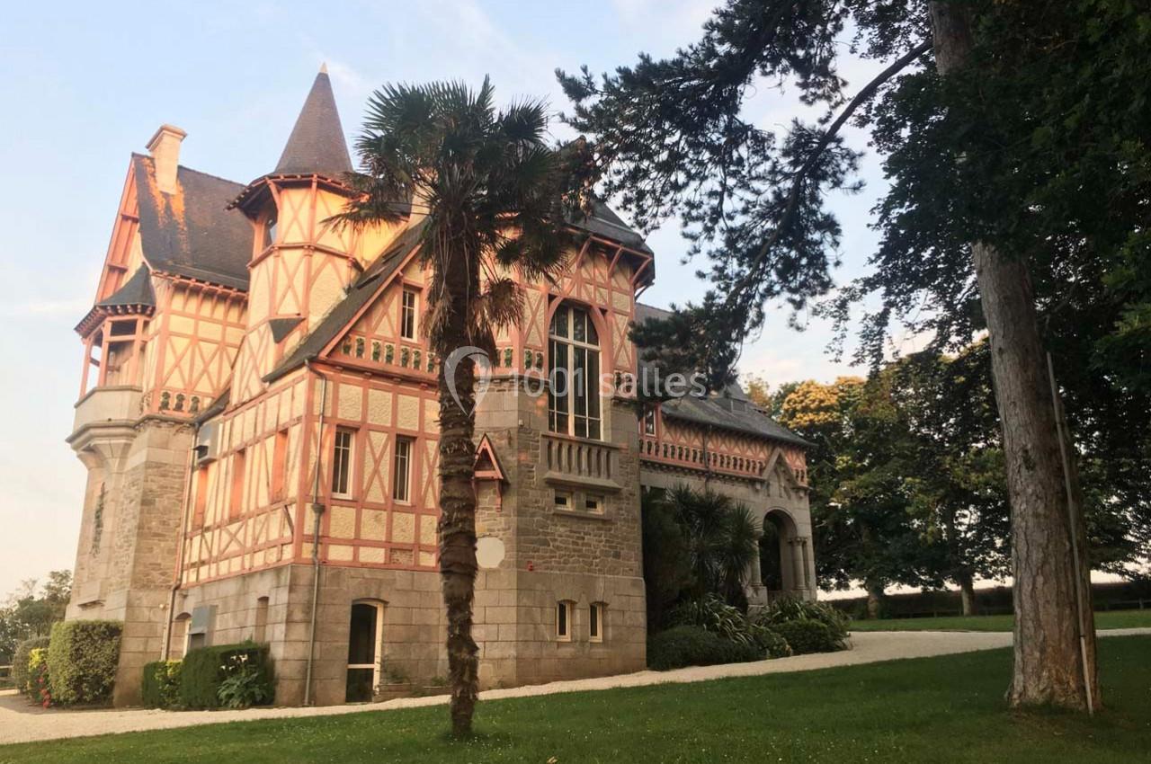 Manoir en pierre et bois à colombages, entouré d'arbres, sous un ciel dégagé en fin de journée.