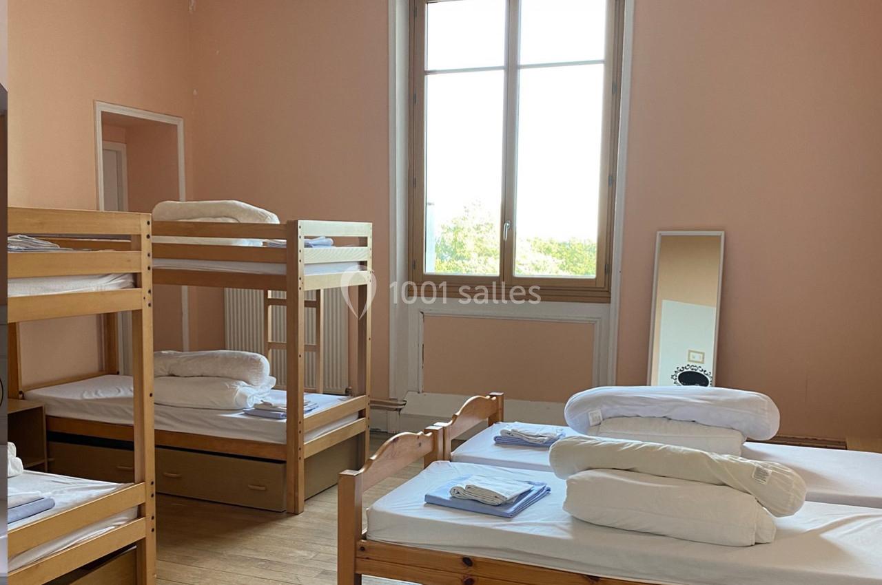 Chambre avec lits superposés et simples, draps pliés, grande fenêtre et miroir posé au sol.