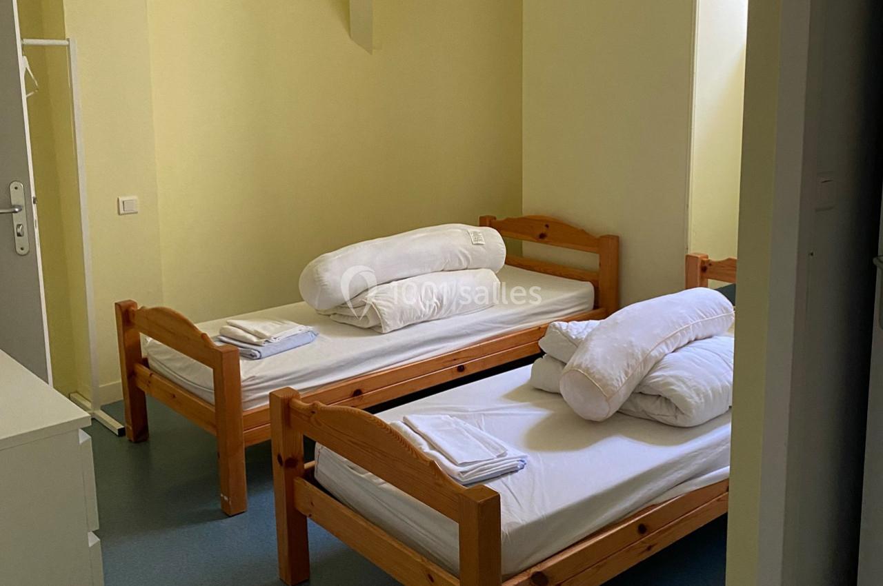 Deux lits simples en bois avec draps et oreillers blancs dans une chambre aux murs jaunes.