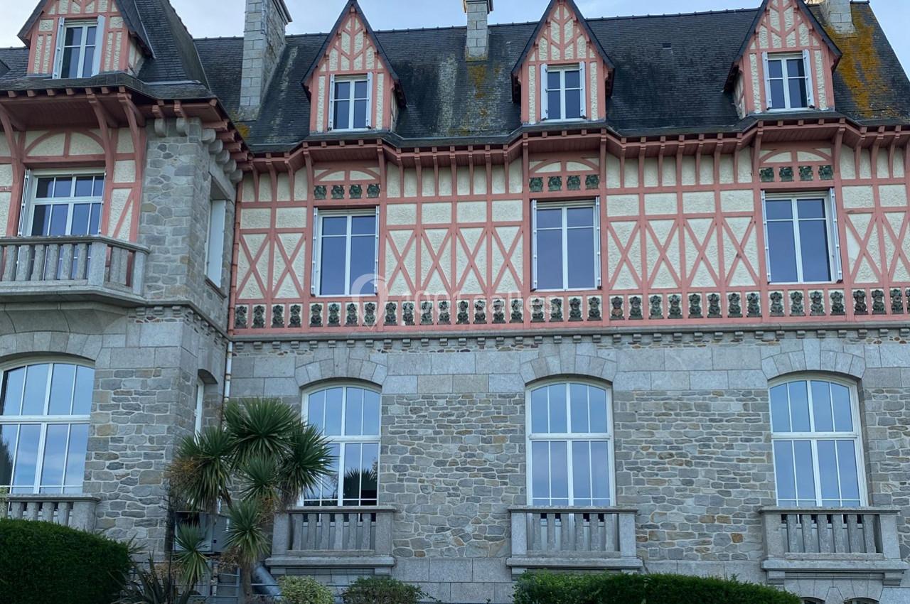 Façade d'une grande maison en pierre avec colombages roses, fenêtres à croisillons et toiture en ardoise.