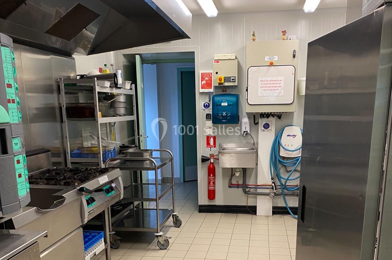 Cuisine professionnelle équipée avec plaques de cuisson, étagères, réfrigérateur, évier et équipements de sécurité visibles.