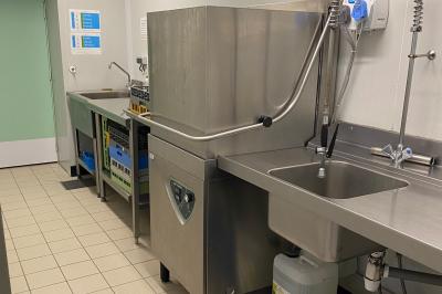 Cuisine professionnelle équipée avec plaques de cuisson, étagères, réfrigérateur, évier et équipements de sécurité visibles.