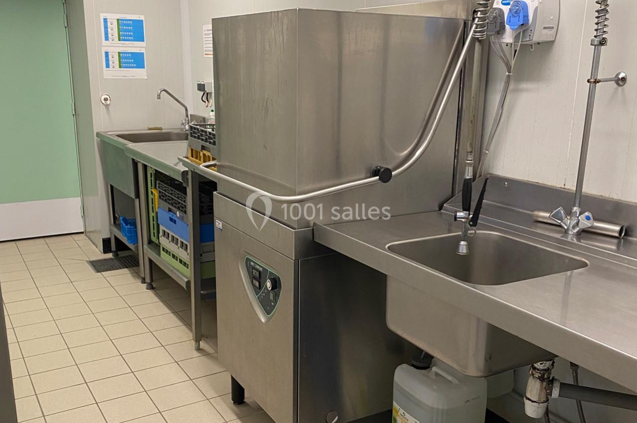 Cuisine professionnelle avec un lave-vaisselle industriel, un évier en inox et des plans de travail en acier.