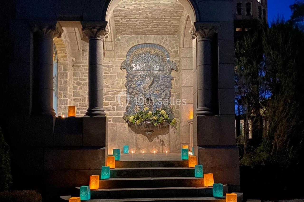 Escalier en pierre illuminé par des lanternes colorées, menant à une alcôve ornée d'une sculpture en relief.