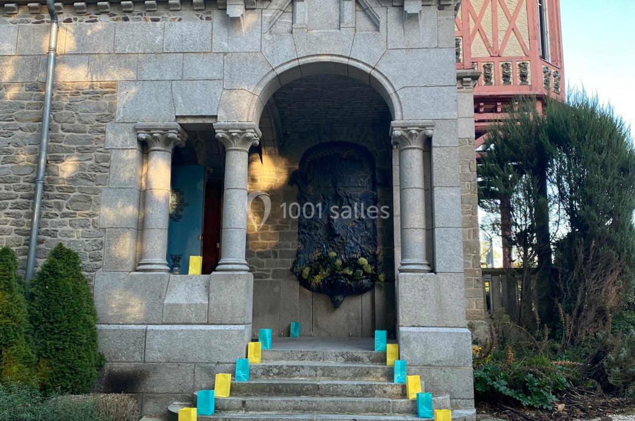 Entrée en pierre avec colonnes, décorée de bougies colorées sur les marches et d'une sculpture murale sombre.