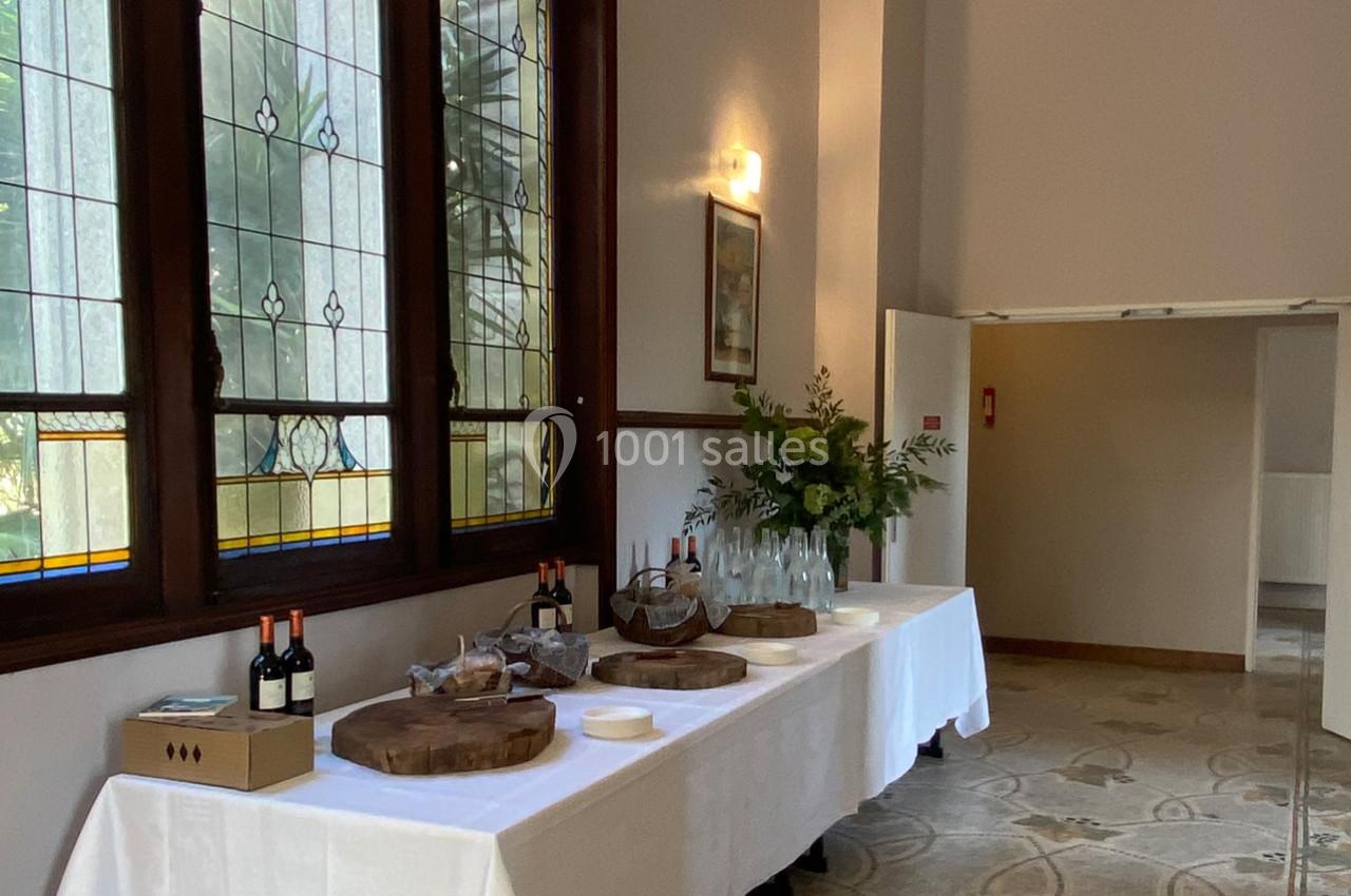 Table dressée avec des bouteilles de vin, des carafes d'eau, des assiettes et des plateaux en bois dans une salle lumineuse.