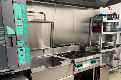 Cuisine professionnelle équipée avec plaques de cuisson, étagères, réfrigérateur, évier et équipements de sécurité visibles.