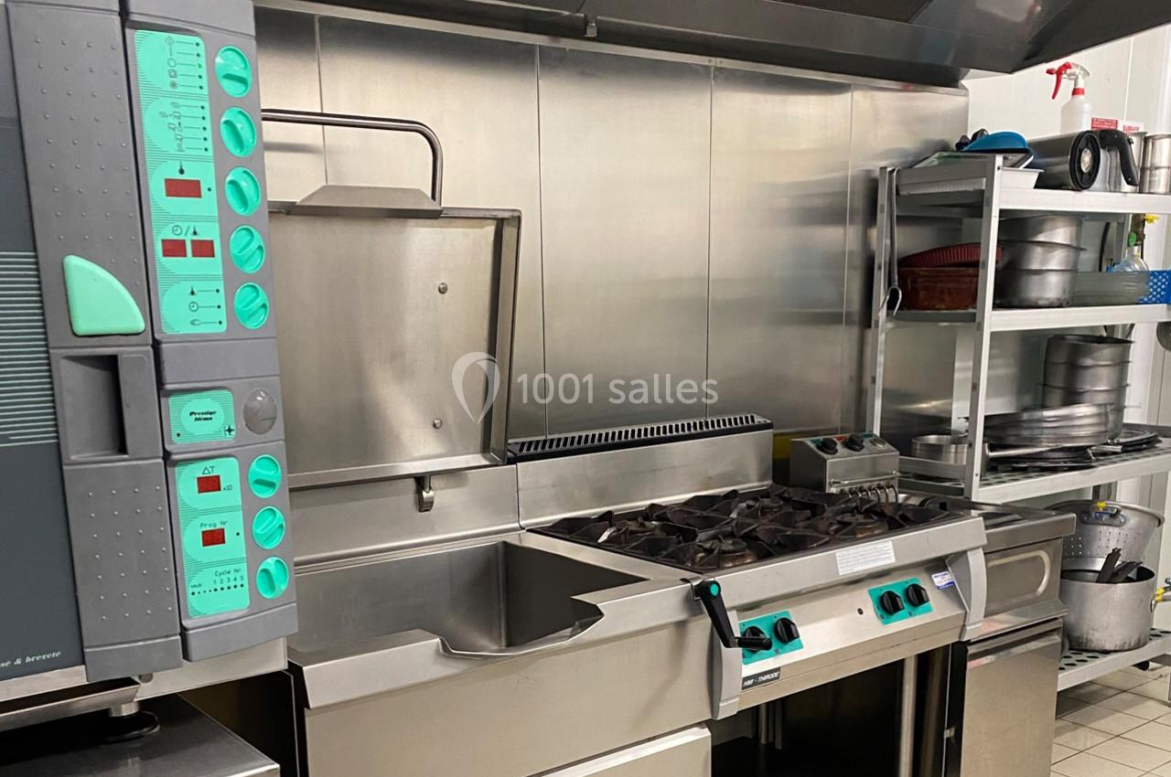 Cuisine professionnelle équipée de plaques de cuisson, d'un four, d'un évier et d'étagères de rangement en inox.