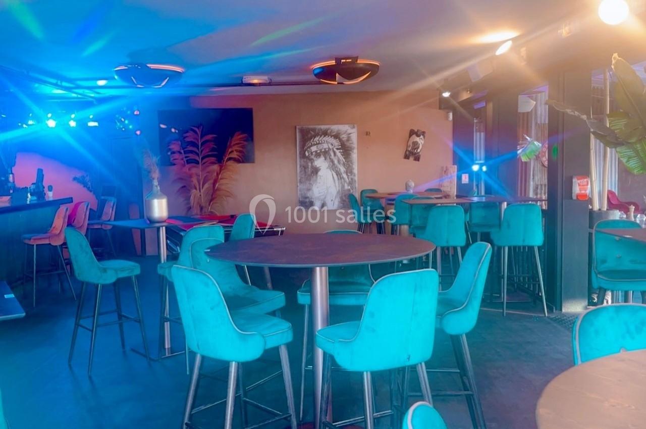 Salle de bar avec tables hautes, chaises turquoise, éclairage coloré et décorations murales modernes.