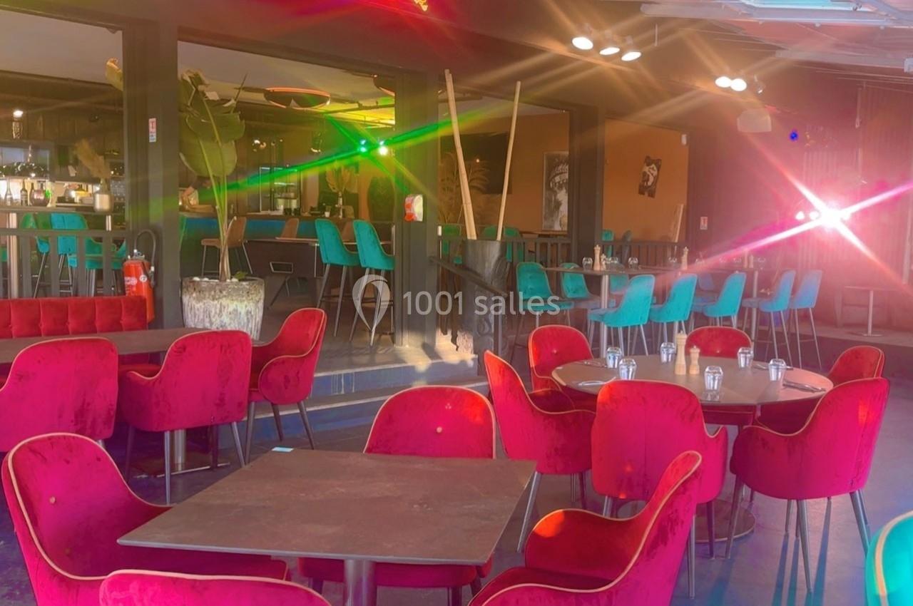 Salle de restaurant lumineuse avec des chaises rouges et turquoise, tables en bois et un bar en arrière-plan.