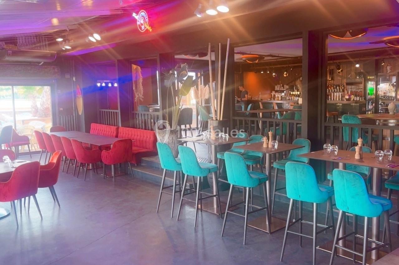 Salle de restaurant moderne avec tables en bois, chaises colorées et bar en arrière-plan.