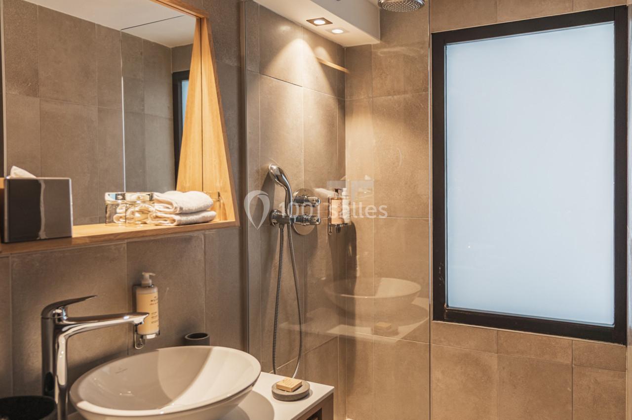 Salle de bain moderne avec douche à l'italienne, lavabo blanc, miroir encadré en bois et fenêtre opaque.