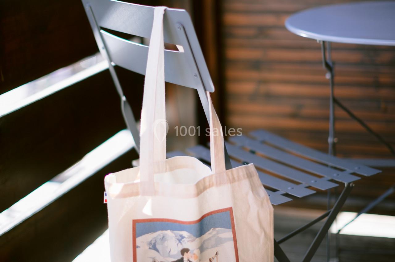 Sac en toile avec illustration de skieurs suspendu à une chaise en métal sur une terrasse en bois.