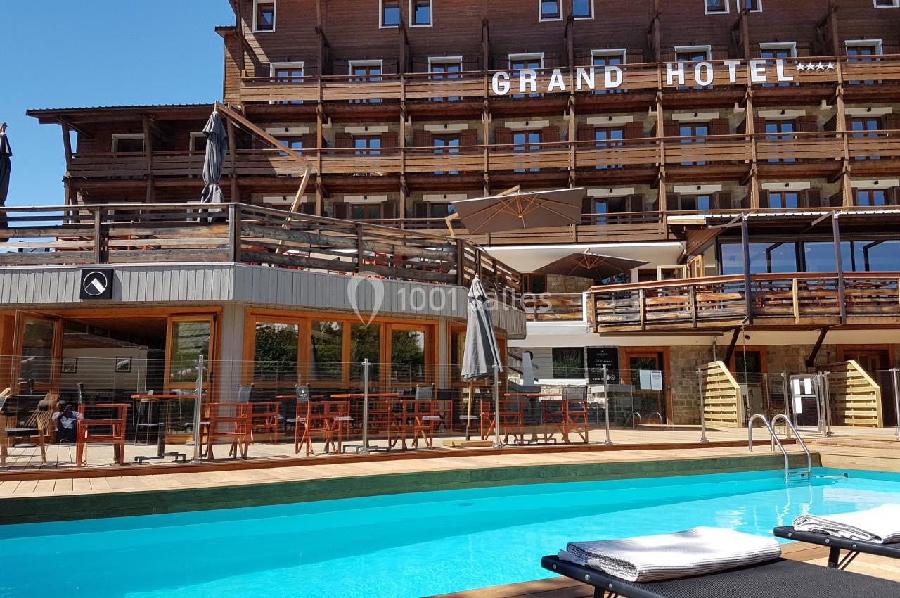 Piscine extérieure avec transats devant un grand hôtel en bois à plusieurs étages, par temps ensoleillé.